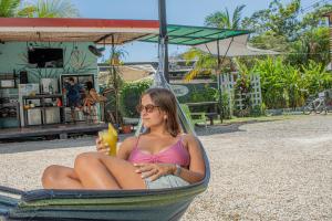 a woman sitting in a hammock with a drink at Habitat Surf Glamp in Santa Teresa Beach