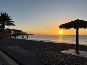 a sunset on a beach with an umbrella and the ocean at Residencial Santo António in Santa Cruz +28 photos