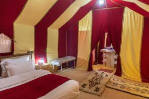 a bedroom with a tent with a bed and a bench at Merzouga dunes erg chabbi Camp in Merzouga