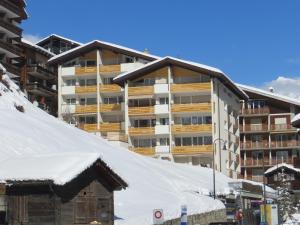 un grand bâtiment dans la neige avec des toits recouverts de neige dans l'établissement Haus Sonnheim, à Zermatt