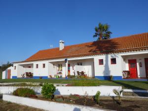 a white house with a red door and a palm tree at Herdade Do Pessegueiro in Porto Covo