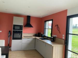 eine Küche mit orangefarbenen Wänden und weißen Schränken in der Unterkunft Les Petites Maisons dans la Prairie - 2 in Maresville