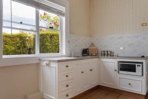 a kitchen with white cabinets and a microwave and two windows at Arendon Cottage in Evandale +3 photos