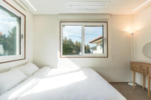 a white bedroom with two beds and a window at Jeju Stone Courtyard Pension in Jeju