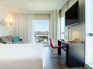 a hotel room with a bed and a desk with a television at Novotel Barcelona City in Barcelona