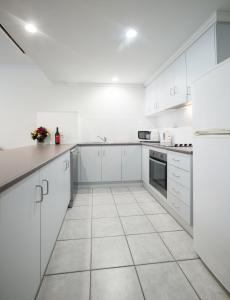 a white kitchen with white cabinets and a tile floor at Franklin Apartments in Adelaide