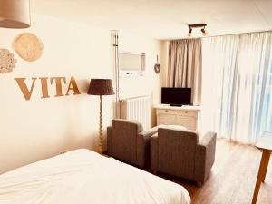 a bedroom with a bed and two chairs and a tv at Casa Al Mare Studio in Zoutelande