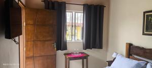 a bedroom with a window with black curtains and a table at Chalés Vitória in Cunha