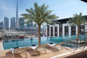 a swimming pool with chairs and palm trees on a building at La Ville Hotel & Suites CITY WALK Dubai, Autograph Collection in Dubai