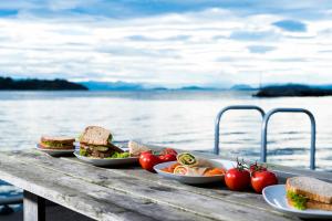 three plates of sandwiches and tomatoes on a table by the water at Sjøberg Hotell og Ferie Leiligheter in Østhusvik