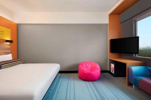 a bedroom with a bed and a tv and a pink chair at Aloft Kuala Lumpur Sentral in Kuala Lumpur