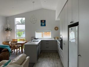 a kitchen with white cabinets and a table with a couch at Guacamole Cottage in Tauranga