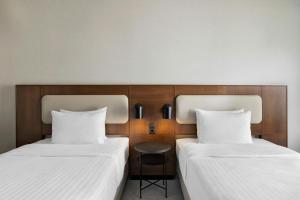 two beds with white sheets and a stool between them at Courtyard by Marriott Munich City East in Munich