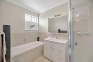 a white bathroom with a tub and a sink and a shower at 4 Bedroom Peaceful stay in Wright with plenty of room to be with family or friends in Weston Creek +7 photos