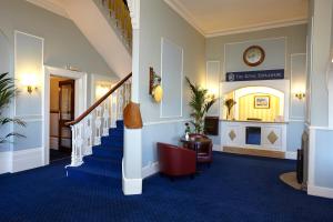 a hallway with blue carpet and stairs with a clock on the wall at Royal Esplanade Hotel in Ryde