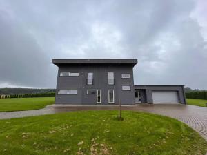 a large gray house with a driveway in a field at Mārtiņmāja in Saraiķi