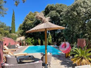 een grote rieten parasol naast een zwembad bij Jolie annexe du mas dans le cœur de la garrigue nîmoise in Nîmes