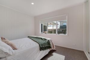 a white bedroom with a bed and a window at Mount Central Hideaway in Mount Maunganui