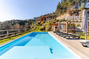 a swimming pool with chairs and umbrellas next to a house at Casa do Sol com Piscina and Sauna para 6 Pessoas in Celorico de Basto