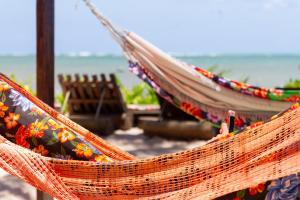 an orange hammock with flowers on it next to the ocean at Pousada Vila do Patacho in Pôrto de Pedras