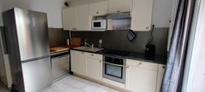 a kitchen with white cabinets and a stainless steel refrigerator at Maison cosy au bord du canal, piscine et parking in Béziers