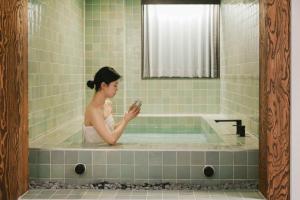 a woman sitting in a bath tub holding a camera at Stay Passport Sindang Ryokan in Seoul