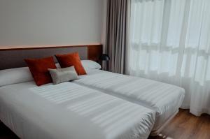 Un dormitorio con una cama con sábanas blancas y almohadas naranjas. en Apartamentos 2H LIVING, en León