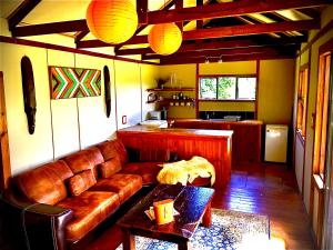 a living room with a brown leather couch and a table at Pura Vida Forest Cabin in Witelsbos