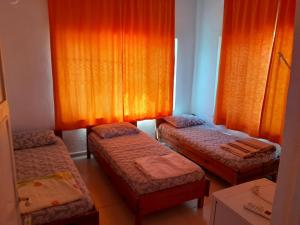 three beds in a room with orange curtains at Huzur Pansiyon in Aydıncık