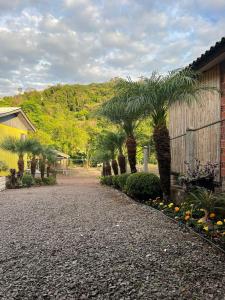 a gravel driveway with palm trees and flowers next to a building at Casa agradável, próximo a Gramado in Três Coroas