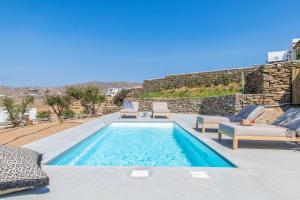 a swimming pool with chaises and chairs next to a stone wall at Rockaine Suites Horizon in Tinos