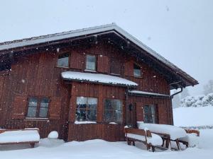 a wooden cabin with snow covered benches in front of it at Ferienhaus Biberweg im Feriendorf Reichenbach 13 in Nesselwang