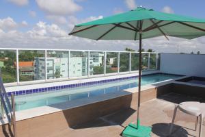 - une piscine avec un parasol vert, une table et une chaise dans l'établissement Flat Makaranduba Centro Porto de Galinhas,dois quartos, à Porto de Galinhas