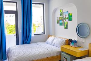 a bedroom with a bed with blue curtains and a window at Sand Sea Hotel Phan Thiết in Phan Thiet