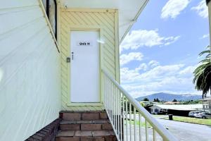 a white door on a yellow house with a stairs at Unit 11 Fenton Summer Lodge Rotorua in Rotorua