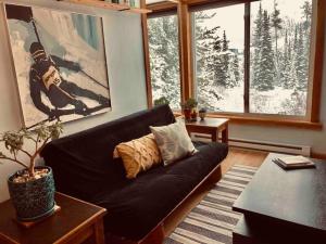 a living room with a black couch in front of a window at Ski Bunny Studio Walkable to Ski Lifts in Big Sky
