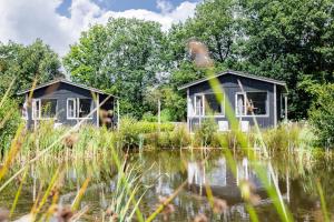 two houses on a lake with trees in the background at Tiny house XL - Vakantiepark De Kremmer in Gasselte