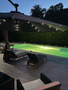 a tennis court under an umbrella with chairs and a table at BY NEPTUNE - La Maison Courtenay Piscine Privée, 4 Chambres in Courtenay