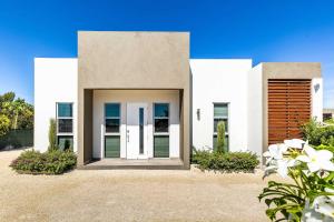a white house with white doors and flowers at Romantic Escape, Walk to Beach, Pool, Hammock in Long Bay Hills