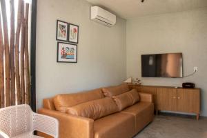 a living room with a brown couch and a flat screen tv at Paraíso Patacho Riviera Casa 01 Villa 04 in Pôrto de Pedras