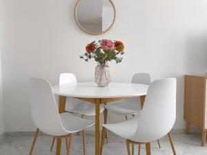ein Tisch mit weißen Stühlen und einer Vase mit Blumen in der Unterkunft Apartamento acogedor - piscina - parking in Sevilla