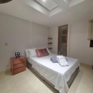 a white bedroom with a bed and a wooden dresser at Infante Loft 402P - WAIWA HOST in Bucaramanga