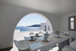 una sala da pranzo bianca con tavolo e vista sull'acqua di CasaDei Pool 4-BDR Sea View Villas 'Anemos' & 'Petra' with Nighttime Security Guard a Panormos - Mykonos