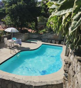 uma piscina com mesa, cadeiras e guarda-sol em CASA a 550 METROS DA SAÍDA DOS PASSEIOS DE BARCO NA PRAIA DOS ANJOS 1 VAGA DE GARAGEM em Arraial do Cabo