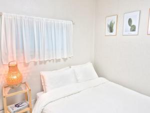 a white bedroom with a bed and a window at Oiso Stay in Busan