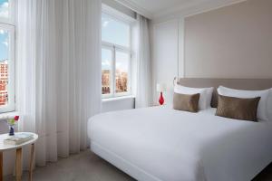a white bedroom with a large white bed and a window at Tivoli Doelen Amsterdam Hotel in Amsterdam