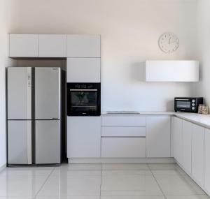 a white kitchen with a refrigerator and a clock at פנטהאוז העצמאות in Qiryat Ata
