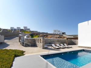 a swimming pool with lounge chairs next to a building at The Mykonian Sunset Villas - 10min from Town in Agios Ioannis Mykonos