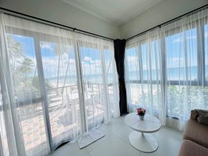 a living room with a table and large windows at Cozy Khanom โคซี่ ขนอม in Ban Na Dan