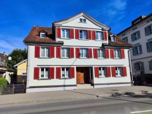 a large white building with red shutters on a street at Schöne Wohnung im Herzen von Herisau bis 6 Gäste in Herisau